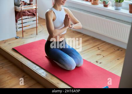 Slim lady in top and leggings sits holding hands in namaste at yoga training on balcony Stock Photo