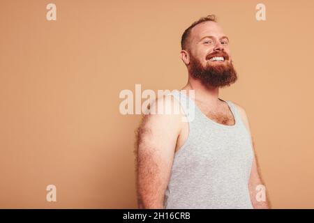 Man with a ginger beard smiling at the camera cheerfully. Body positive young man standing against a studio background. Self-assured young man feeling Stock Photo