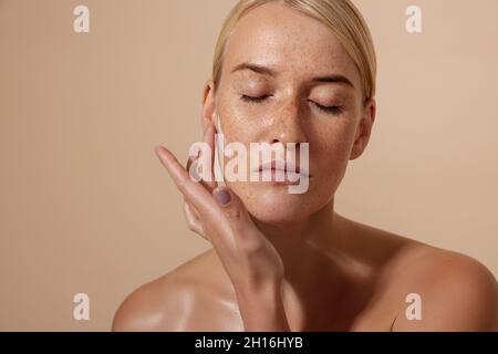 Beautiful female applying moisturizer on face in studio Stock Photo