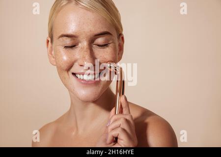 Happy woman using facial roller. Young female doing skincare routine. Stock Photo