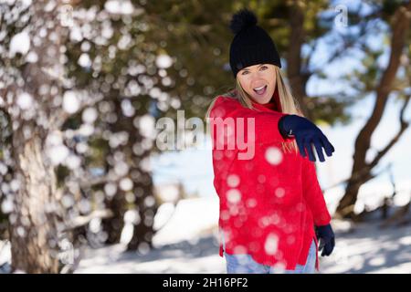 Blonde woman throwing snowballs forward in a snow-covered forest in the mountains Stock Photo