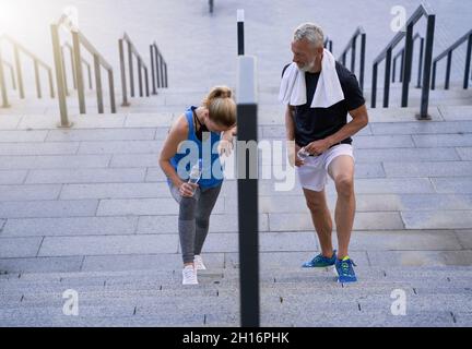 Tired middle aged couple, man and woman in sportswear walking up the stairs after exercising together outdoors Stock Photo