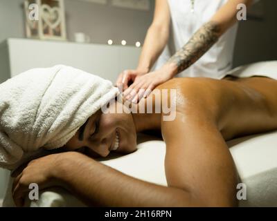 Unrecognizable female masseur massaging back of client in towel on couch in light spa center Stock Photo
