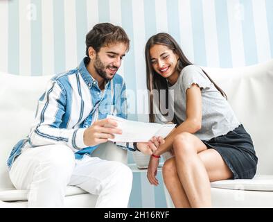 man and smiling Woman sitting on white armchairs and looking at brochure in salon Stock Photo