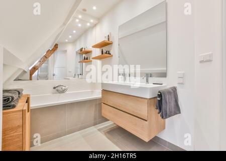 Interior of modern bathroom with bathtub and wooden furniture in mansard of spacious house Stock Photo
