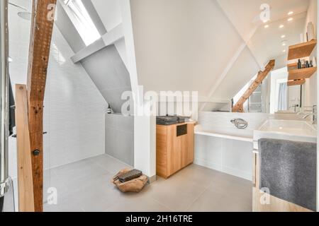 Interior of contemporary bathroom with white tiled walls and ceramic sink in mansard in daylight Stock Photo