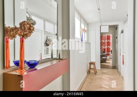 Corridor with windows and colorful decorated vases leading to room with armchairs in light apartment with white walls and wooden chair Stock Photo
