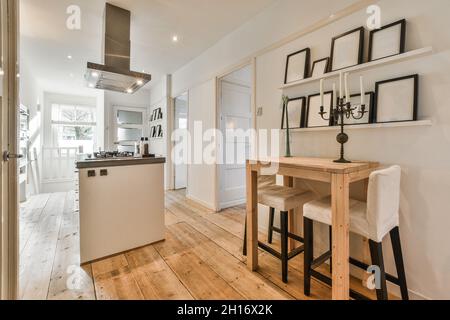 Modern kitchen with hood above gas stove against frames on shelves over candelabrum on wooden table in light house Stock Photo