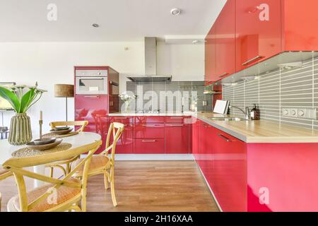 Modern interior of kitchen with red cabinets and white dining table decorated with flowers in vase in contemporary apartment Stock Photo