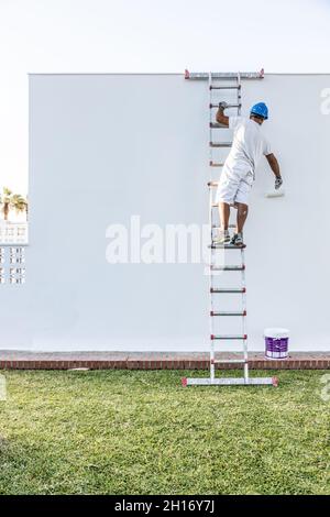 Unrecognizable young painter painting the facade of an apartment with a roller from the staircase Stock Photo