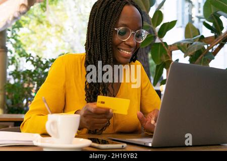 Young curly haired ethnic female student in casual outfit with glass of juice in hand reading feed news in social networks on mobile phone while chill Stock Photo