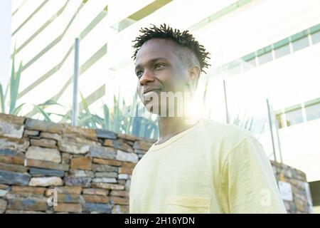 From below positive African American young male wearing casual clothes standing standing near stone wall Stock Photo