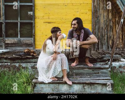 Hippie man watching a beautiful hippie Woman drinking from a cup on a wooden porch Stock Photo