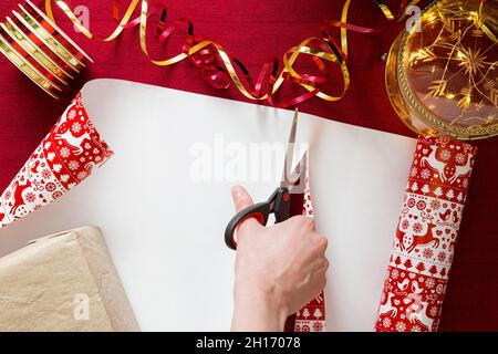 Family preparing for Christmas. Top view of hands wrapping gifts. Boxes with presents, colorful wrapping paper, scissors and ribbons. Stock Photo