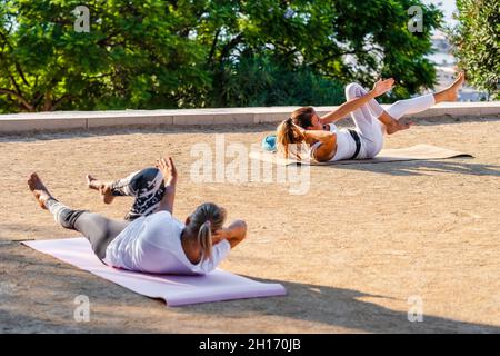 Sportive ladies lying on mats on terrace against trees and doing crunches together in daylight Stock Photo
