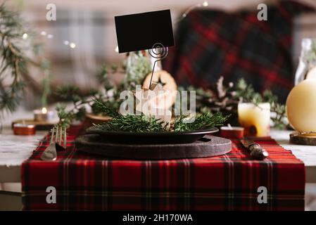 Christmas table setting with reindeer of wood with blank name card on ceramic plate on red checkered tablecloth on the background Stock Photo