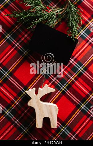 Christmas Reindeer of wood with blank name card on red checkered fabric and decorative pine wreath. Stock Photo