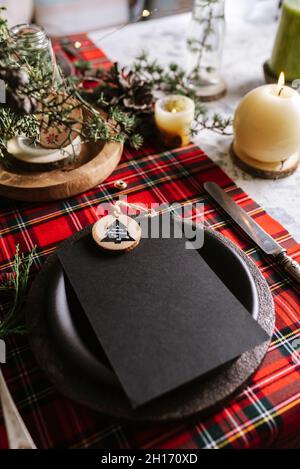 Top view of christmas table setting with empty menu on ceramic plate and red checkered tablecloth with yellow lights on the background Stock Photo
