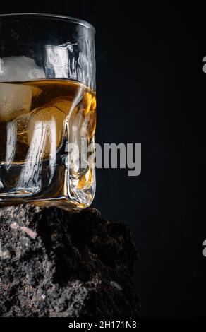 Whiskey with ice cubes served in crystal glass placed on rough surface against black background Stock Photo
