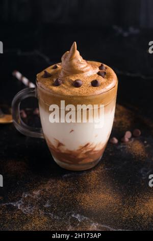 From above glass of sweet Dalgona coffee with foamy topping served on table with chocolate wafer roll and cocoa powder Stock Photo