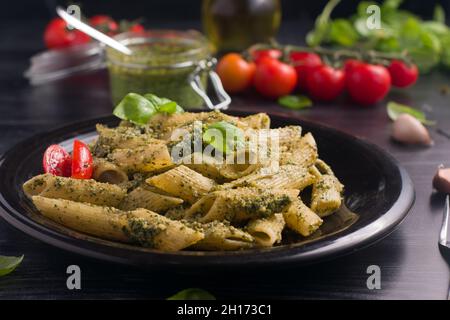 Close- up plate with delicious pasta with green pesto sauce and tomatoes served on black wooden table Stock Photo