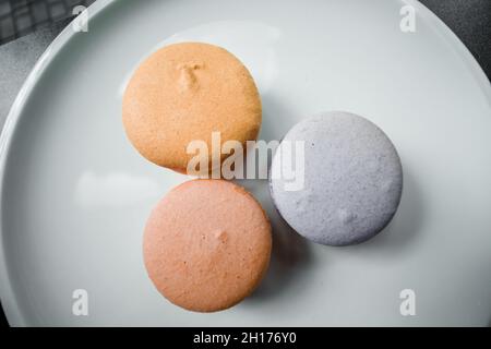 Three macaroon cookies lie on a white plate in a pastry shop. Stock Photo