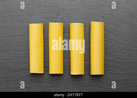 Raw dried cannelloni pasta, a tubular pasta that is usually stuffed with meat or vegetables, on a black background. Italian cannelloni pasta tubes. To Stock Photo