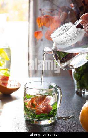 A healthy hot drink with mint and grapefruit, pouring hot water from glass teapot into glasses, aromatic mint tea with citrus fruits Stock Photo