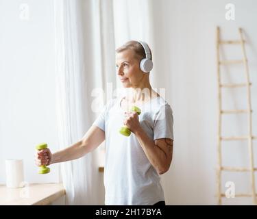 Portrait of happy senior woman doing fitness exercise with dumbbells at home Stock Photo