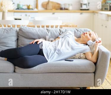 Mature woman listening to headphones music laying upon sofa and dreaming with closed eyes Stock Photo