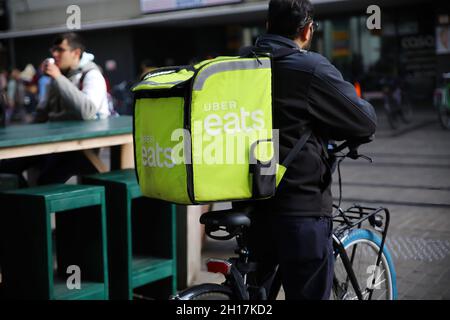 Ghent, Belgium - October 9. 2021: Closeup of uber eats food deliver service person on bicycle with green back pack in city centter (focus on front of Stock Photo