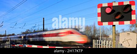 Azuma train passing Red lights at an unmanned Level crossing, East Coast Main Line Railway, Peterborough, Cambridgeshire, England, UK Stock Photo