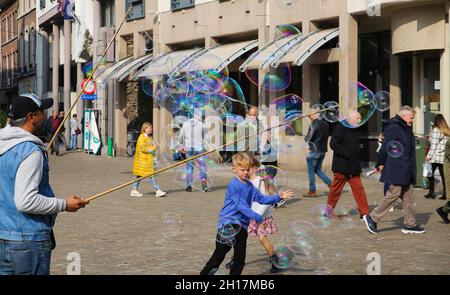 Ghent, Belgium - October 9. 2021: Children burst soap bubbles made by showman with two sticks on city street Stock Photo