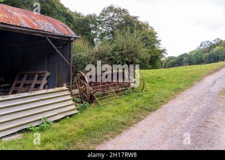 old disused farm machinery industrial equipment abandoned next to a modern metal barn Stock Photo