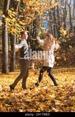 Leisure, relationship concept. Lovely couple enjoy autumn in falling maple tree leaves foreground during sunny day. Bright vivid backlight filter. Man Stock Photo