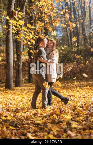 Leisure, relationship concept. Lovely couple enjoy autumn in falling maple tree leaves foreground during sunny day. Bright vivid backlight filter. Fac Stock Photo