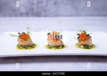 Scallops with caviar, microgreens and green sauce on a white plate. Close-up. Stock Photo