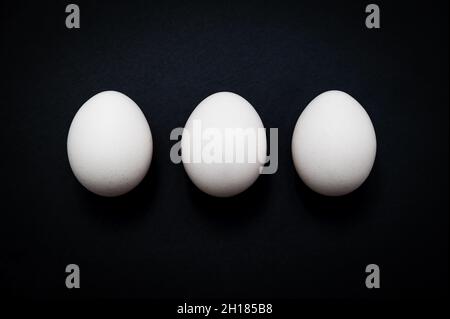 Horizontal breakfast triple: three white chicken eggs against a dark slate background. Stock Photo