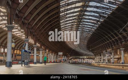 A panorama of a railway station concourse.  An 19h century iron canopy curves above the platforms and the sunlight falls on the platform.  A footbridg Stock Photo