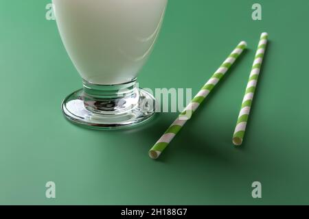 Two stripped paper straws near footed glass of milk white cocktail over green background. Pair of disposable cardboard drinking tubes and glass of bev Stock Photo