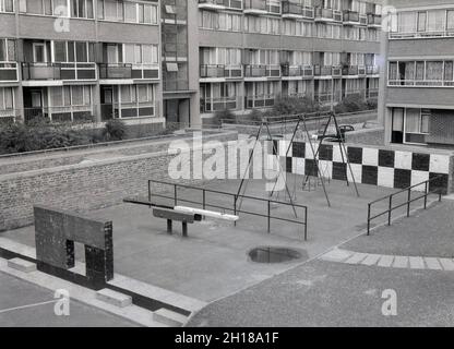 1960s, historical, a concrete and walled playground area, at a large council housing estate, Churchill Gardens in Pimlico, inner London, England, UK. Built between 1948 and 1962 to replace victorian terraces damaged in the Blitz of WW2, this was a huge estate of social housing, with 32 tower blocks providing 1,600 homes. Outside the flats, in the walled, concrete built enclosure, traditional playground equipment with swings and see-saw. Stock Photo