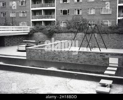 1960s, historical, a concrete and walled playground area, at a large council housing estate, Churchill Gardens in Pimlico, inner London, England, UK. Built between 1948 and 1962 to replace victorian terraces damaged in the Blitz of WW2, this was a huge estate of social housing, with 32 tower blocks providing 1,600 homes. Outside the flats, in the walled enclosure with a concrete base, traditional playground equipment, including swings, a roundabout and see-saw. Stock Photo