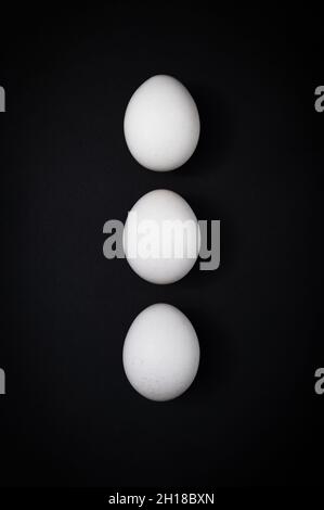 Vertical breakfast triple: three white chicken eggs against a dark slate background. Stock Photo