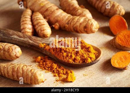 Turmeric powder on a wooden spoon with fresh whole and sliced root in the background Stock Photo