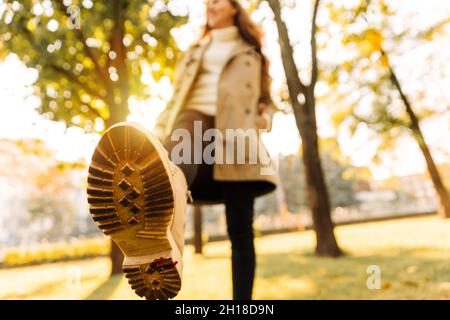 close-up of a woman's autumn shoes walking in a park full of trees with yellow leaves. woman in beige raincoat Stock Photo