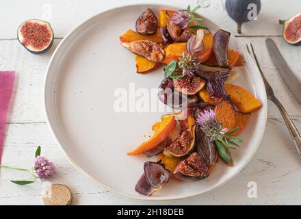Delicious autumn or winter side dish with oven roasted and caramelized pumpkin, red onions and figs. Served on a white plate on wooden table. Stock Photo