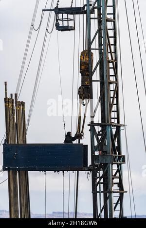 A derrickman or derrickhand on the tubing board on the mast of a workover rig on an oil well in Utah. Stock Photo