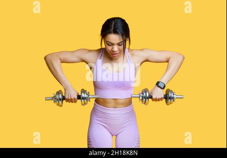Sport concept. Young fit african american woman exercising with two dumbbells, doing arms workout, yellow background Stock Photo