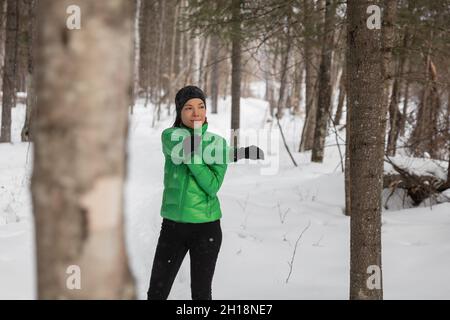 Winter fitness athlete woman warming up stretching arms before her outdoor run running on snow trail. Asian runner wearing cold weather gloves Stock Photo