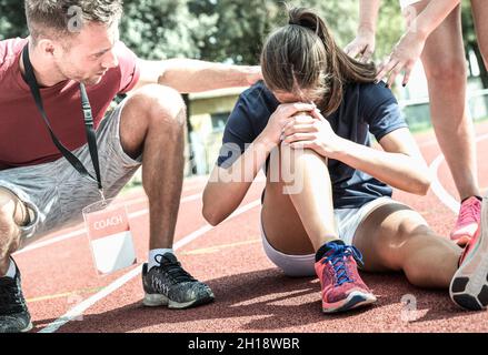 Female athlete getting injured during athletic run training - Male coach taking care on sport pupil after physical accident - Team care concept Stock Photo